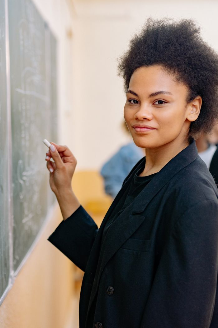 A smiling student writes on a blackboard during a classroom lesson, showcasing education in action.